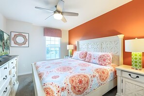A bedroom with a bed, a ceiling fan, a window with blinds, a nightstand with a lamp, and a dresser with drawers. - Colorful 5BR Villa w/ Pool Solara Resort Disney (Kissimmee)