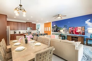 Une cuisine moderne avec des meubles en bois, un coin repas avec une table dressée pour quatre personnes, et un grand écran de télévision diffusant une scène de film.