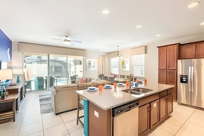 A modern kitchen with a central island, stainless steel appliances, and a view to the outside. - Colorful 5BR Villa w/ Pool Solara Resort Disney (Kissimmee)