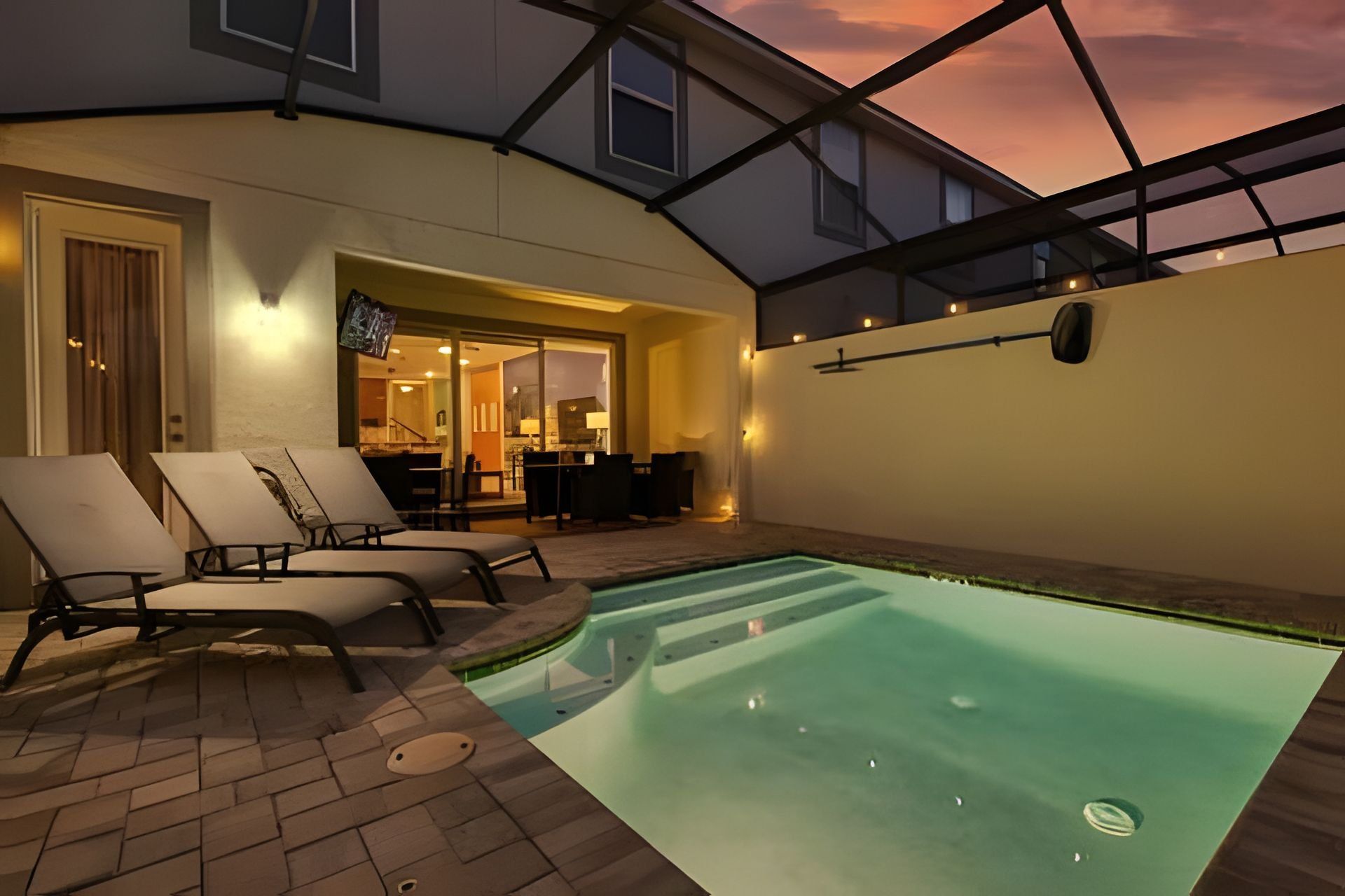 An indoor swimming pool with lounge chairs, a kitchen area, and a glass ceiling.