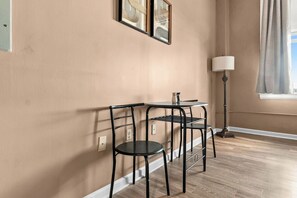 Een kamer met een beige wand, een ronde tafel met een stoel, een vloerlamp en een raam met gordijnen.