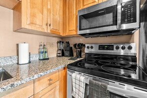 A kitchen with wooden cabinets, a stainless steel microwave, a stove with four burners, and a granite countertop. - Downtown Cleveland 1BR | Walk to Playhouse Square (Cleveland)