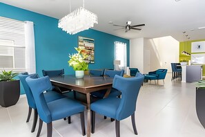 A modern dining area with a round table, blue chairs, and a decorative chandelier. - 6BR Disney Retreat w/ Pool & Themed Rooms (Davenport)
