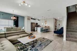 A modern living room with a sofa, coffee table, and a dining area with chairs. - 5BR Storey Lake Townhome, Heated Pool (Kissimmee)