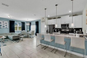 A modern kitchen with white cabinets, a central island with bar stools, and a dining area with a sofa and chairs. - 5BR Storey Lake Townhome, Heated Pool (Kissimmee)