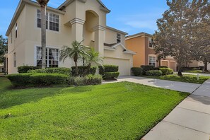 A two-story house with a well-maintained lawn and a driveway leading to the entrance. - Family 6BR Villa w/ Marvel Game Room & Pool (Kissimmee)