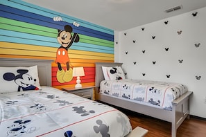 Ein Kinderzimmer mit farbig gestreifter Wand, Bettwäsche mit Mickey Mouse-Motiv und Wandbildern.