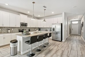 A modern kitchen with white cabinets, a stainless steel refrigerator, a built-in microwave, and a granite countertop. - 6BR Storey Lake Home, Private Pool (Kissimmee)