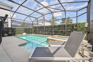 A pool area with a glass enclosure, lounge chairs, and a hot tub. - 6BR Storey Lake Home, Private Pool (Kissimmee)