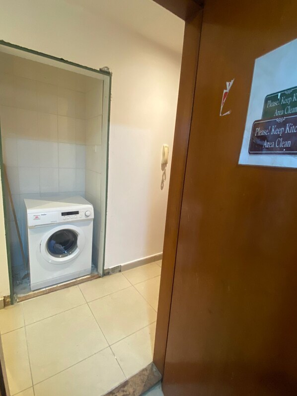 A hotel bathroom with a white washing machine, a glass shower enclosure, and a sign requesting to keep the area clean. - Compact Partition Room in Tecom  (Dubai)