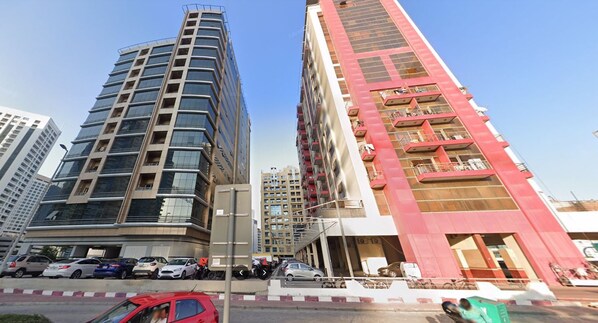 A modern high-rise building with multiple floors, a parking area in front, and a clear sky.