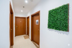 A hallway with wooden doors, a tiled floor, and a green wall decoration. - Compact Partition Room in Tecom  (Dubai)