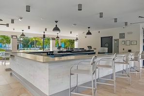 A modern bar area with a central island, bar stools, pendant lighting, and a view of the outdoors. - Modern 4BR Resort Townhome Near Universal (Orlando)