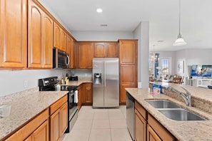 A modern kitchen with wooden cabinets, stainless steel appliances, granite countertops, and a double sink. - Spacious 4BR Condo at Vista Cay Resort (Orlando)