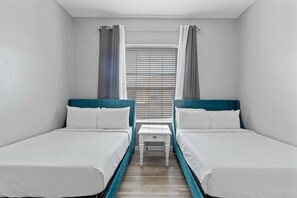 Een kamer met twee eenpersoonsbedden, een klein wit tafeltje en een raam met luxaflex.