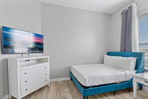 A modern bedroom with a bed, a TV, a dresser, and a window with curtains. - Spacious 4BR Condo at Vista Cay Resort (Orlando)