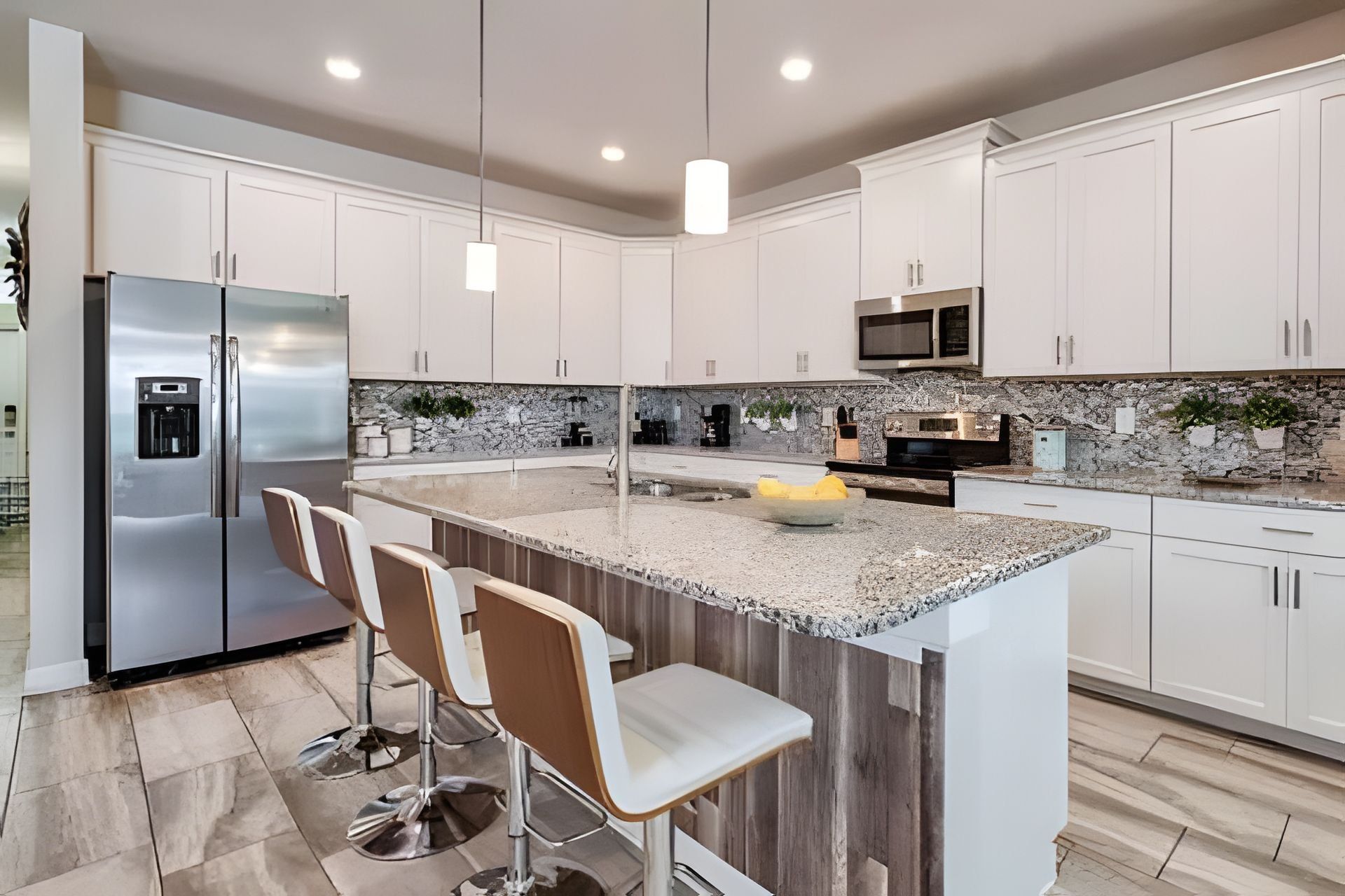A modern kitchen with white cabinets, a stainless steel refrigerator, a granite countertop, and bar stools.
