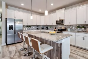 Eine moderne Küche mit weißen Schränken, einem Edelstahl-Kühlschrank, einer Granit-Arbeitsplatte und Barhocker.