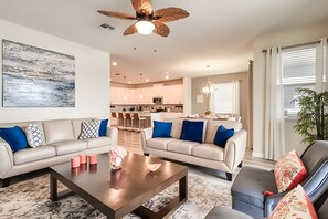 A modern living room with two sofas, a coffee table, and a ceiling fan. - 6BR Pool Home w/ Mickey + Avengers Storey Lake (Kissimmee)