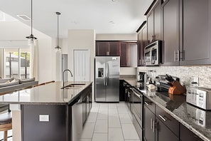 A modern kitchen with stainless steel appliances, dark cabinetry, and a large island with a sink. - 5BR w/ South Pool, Game Room Storey Lake (Kissimmee)