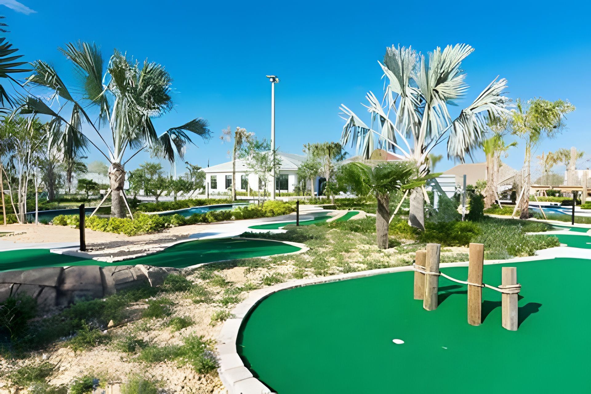 A golf course with a putting green, palm trees, and a building in the background.