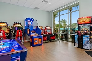 A brightly lit indoor arcade with various gaming machines, including a basketball game, a racing game, and a claw machine. - Disney 5BR Resort Home + Lazy River & Mini Golf (Davenport)