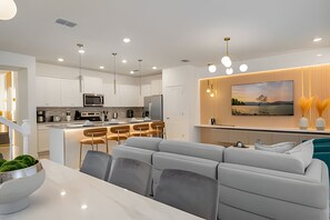 Een moderne keuken met witte kasten, een centraal eiland en een zithoek met een grijze bank en stoelen.