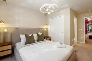 Een hotelkamer met een bed, nachtkastjes, een wandlamp en een deur naar een andere kamer.