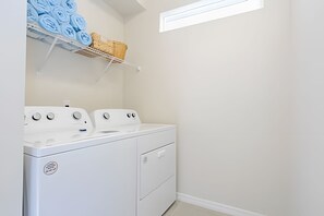 A laundry room with a front-loading washer and dryer, a shelf with folded towels, and a small window. - Windsor Island 5BR Villa w/ Pool & Game Room (Davenport)