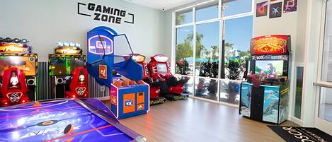 A gaming zone with arcade machines, a pool table, and large windows offering a view of the outdoors.