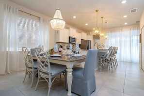 Een moderne eethoek met een grote tafel, witte stoelen en hanglampen.