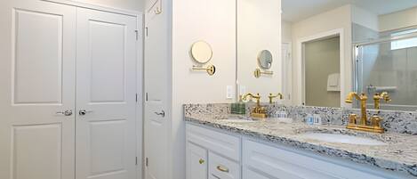 A bathroom with white cabinetry, a marble countertop, gold fixtures, and a large mirror.