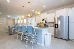 Een moderne keuken met een centraal eiland, roestvrijstalen apparatuur en een eethoek met stoelen.