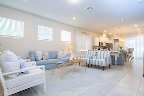 A modern living room with a sofa, armchairs, and a coffee table. There is a kitchen area in the background with a dining table and chairs. - Windsor Island 5BR Villa w/ Pool & Game Room (Davenport)