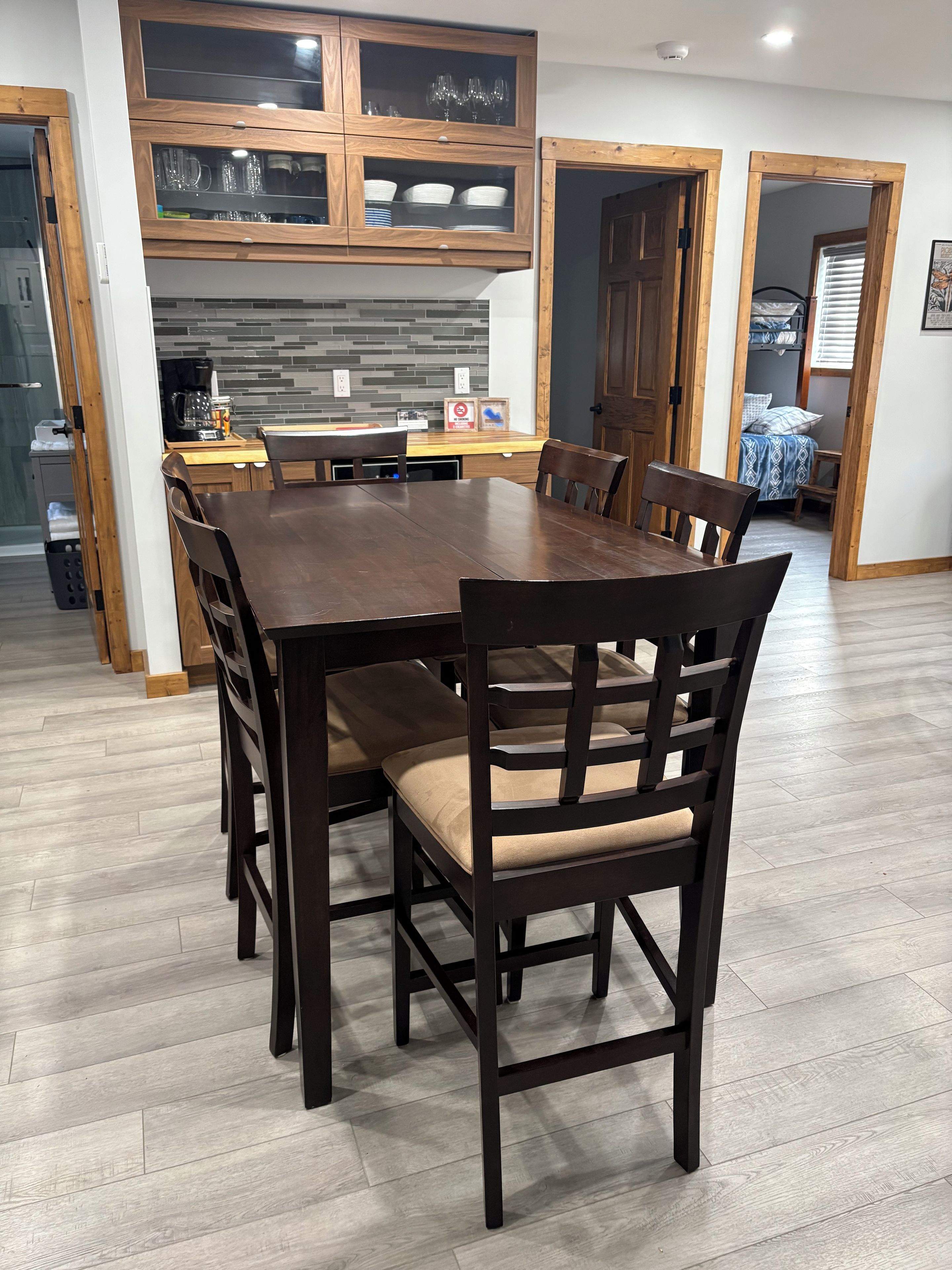 Un comedor con mesa y sillas de madera, una cocina con salpicadero de azulejos y un dormitorio visible a través de una puerta abierta.