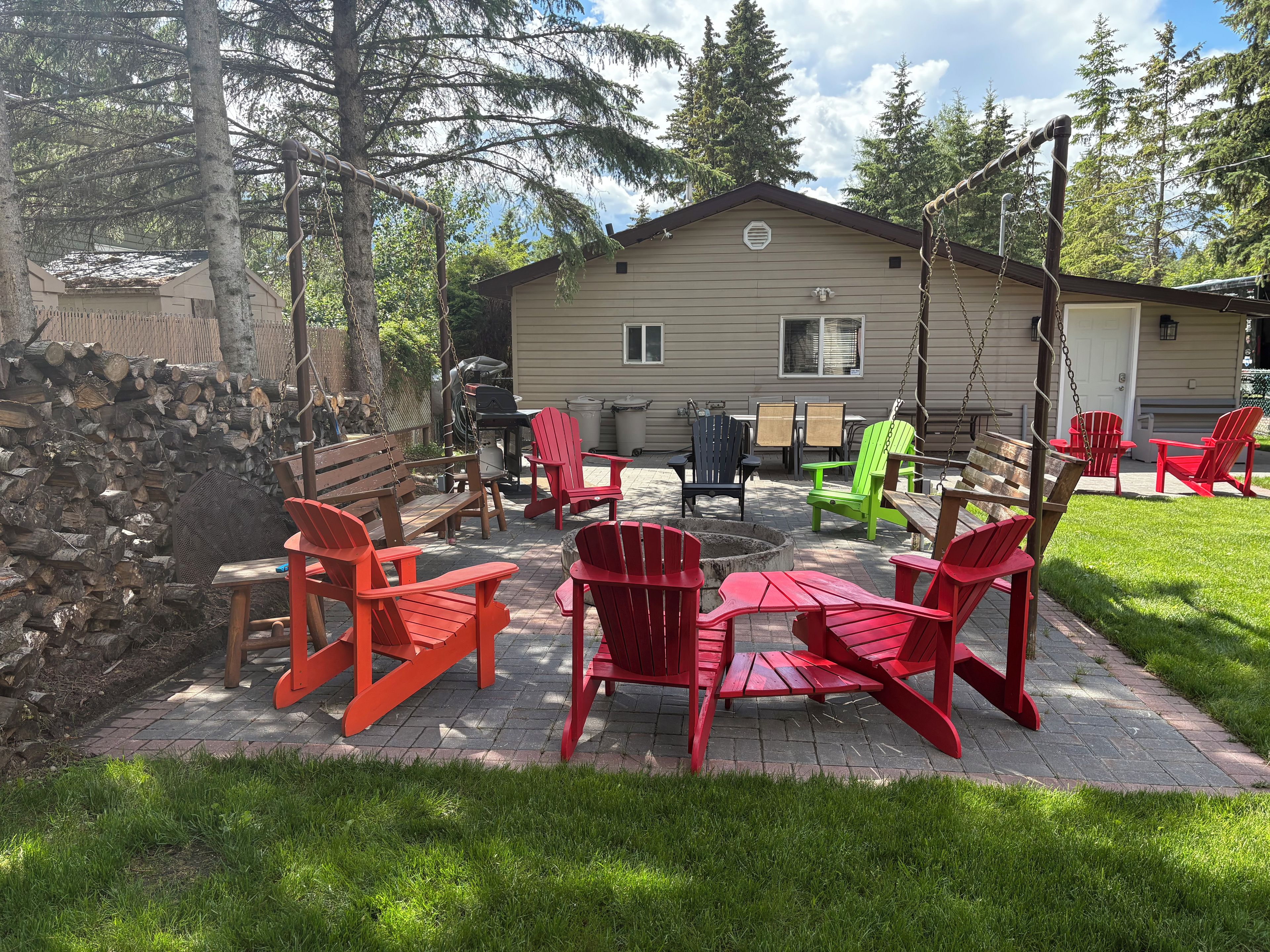 An outdoor patio area with red Adirondack chairs, a wooden table, and a grill.