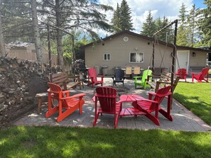 An outdoor patio area with red Adirondack chairs, a wooden table, and a grill.