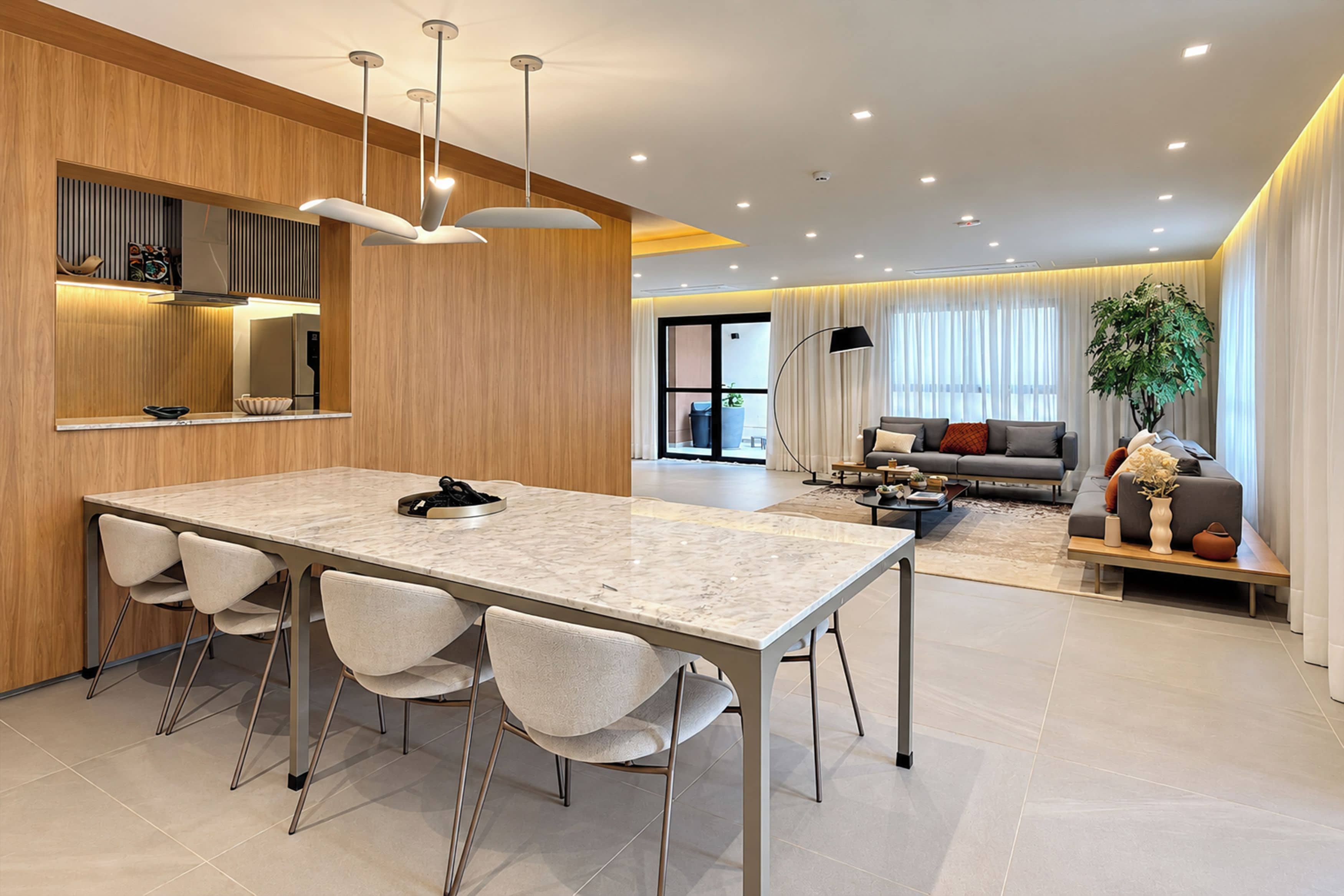 Una cocina moderna con encimera de mármol y cuatro sillas, un comedor con sofá y mesa de centro, y un amplio ventanal con cortinas.