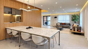 Una cocina moderna con encimera de mármol y cuatro sillas, un comedor con sofá y mesa de centro, y un amplio ventanal con cortinas.