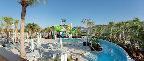 A resort pool area with a water slide, lounge chairs, and palm trees.