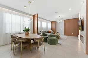 Un salon moderne avec une table à manger ronde en bois, des poufs verts et un canapé agrémenté de coussins.