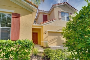 A two-story house with a yellow facade, a red door, and a garage. - Luxury 7BR Home w/ Pool & Spa Near Disney (Davenport)