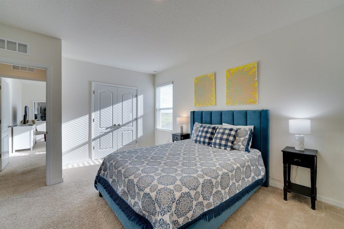 A bedroom with a large bed, a nightstand with a lamp, and two abstract paintings on the wall.
