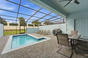 A covered outdoor swimming pool with lounge chairs, a barbecue grill, and a table with chairs. - Modern 5BR Villa w/ Private Pool at Windsor (Kissimmee)