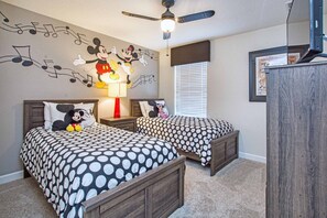 A bedroom with two beds, a Mickey Mouse mural, a ceiling fan, and a window with blinds. - 7BR Home for 15 w/ Private Pool Champions (Davenport)