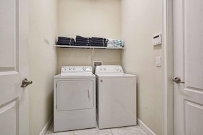 A laundry room with two stacked washers and dryers, a shelf with folded towels, and a door with a handle. - 7BR Home for 15 w/ Private Pool Champions (Davenport)