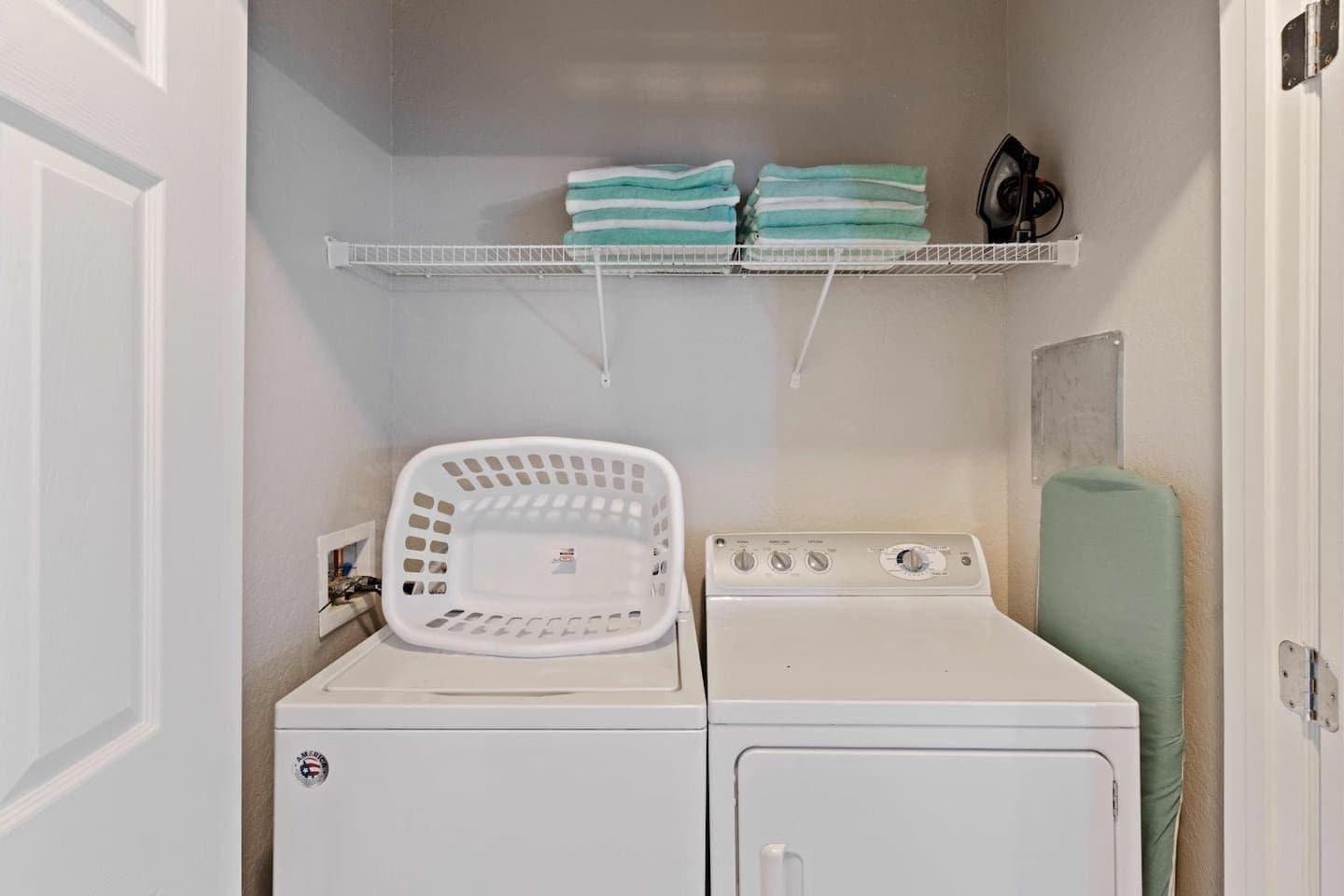 Une buanderie équipée d’un lave-linge à chargement frontal, d’un panier à linge blanc et d’une étagère où sont pliées des serviettes.