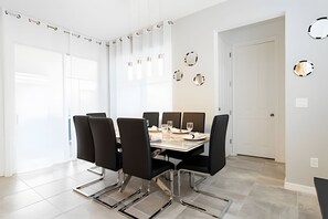 A dining area with a table set for four, surrounded by chairs, in a room with a white door and a wall with circular cutouts. - Solara Resort 6BR Home w/ Pool, Spa & Game Loft (Kissimmee)