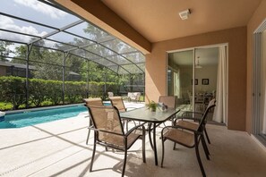 A covered patio with a glass enclosure, a pool, and outdoor furniture. - Bella Vida 6BR Home Near Disney Parks (Kissimmee)