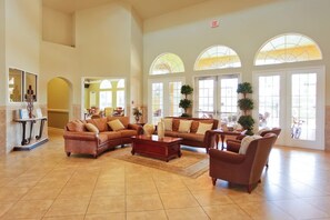 A spacious lobby with high ceilings, large arched windows, and multiple seating areas including sofas and a coffee table. - Bella Vida 6BR Home Near Disney Parks (Kissimmee)